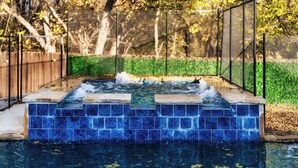 A hot tub with a blue-tiled edge, surrounded by a fence and greenery. - Geyser Ave (Pflugerville)