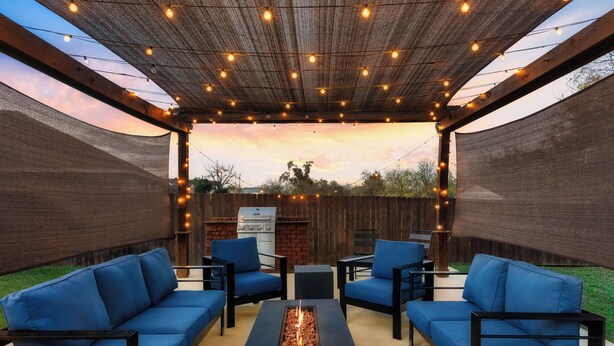 An outdoor patio with a fire feature, blue cushioned seating, and string lights. - Geyser Ave (Pflugerville)
