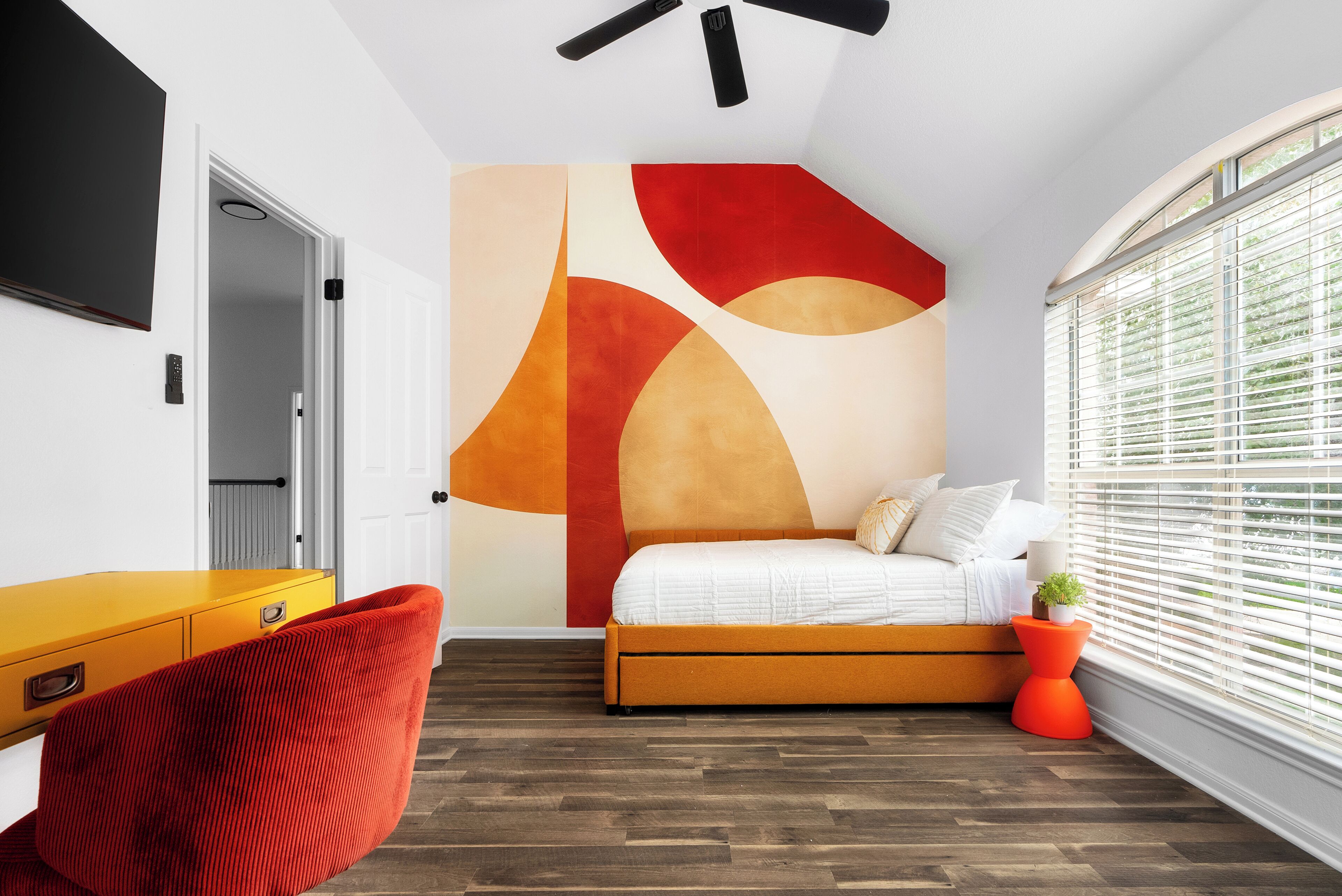 Ein Schlafzimmer mit Bett, Schreibtisch, Stuhl und einem großen abstrakten Wandbild.