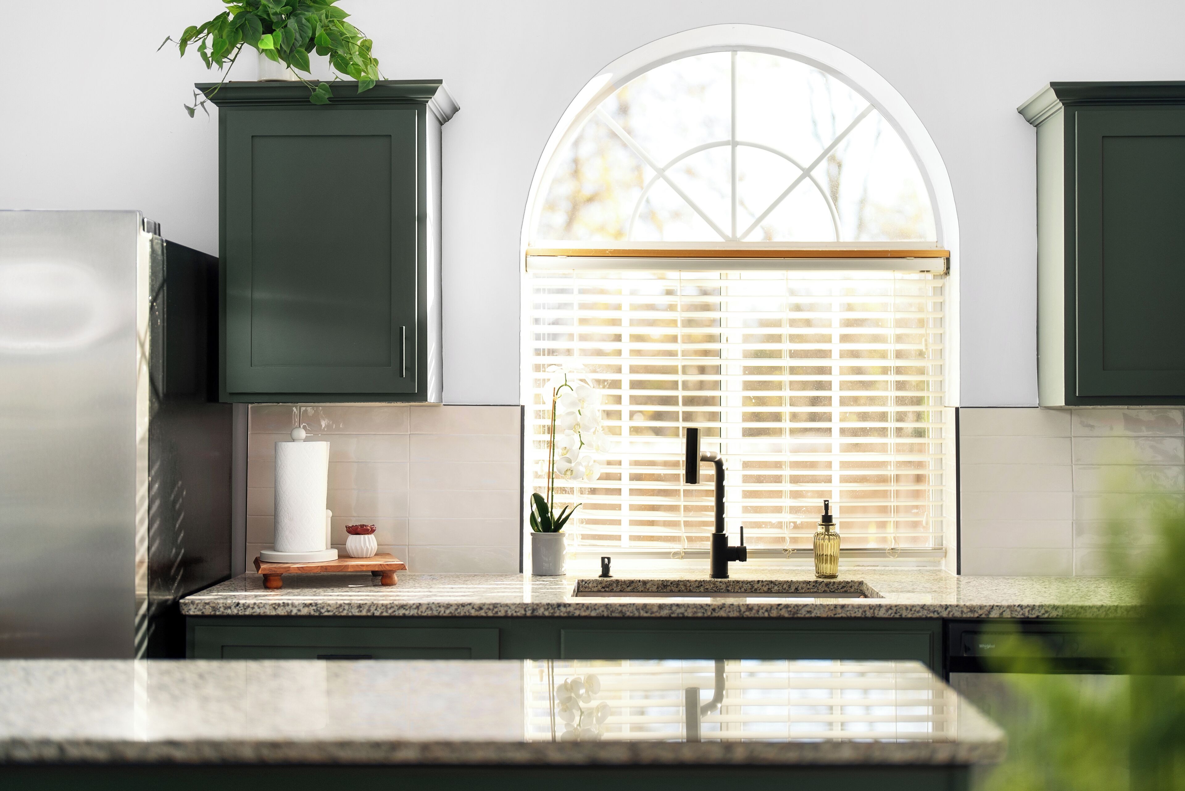 Una cocina con ventana, armarios, un lavamanos y una planta.