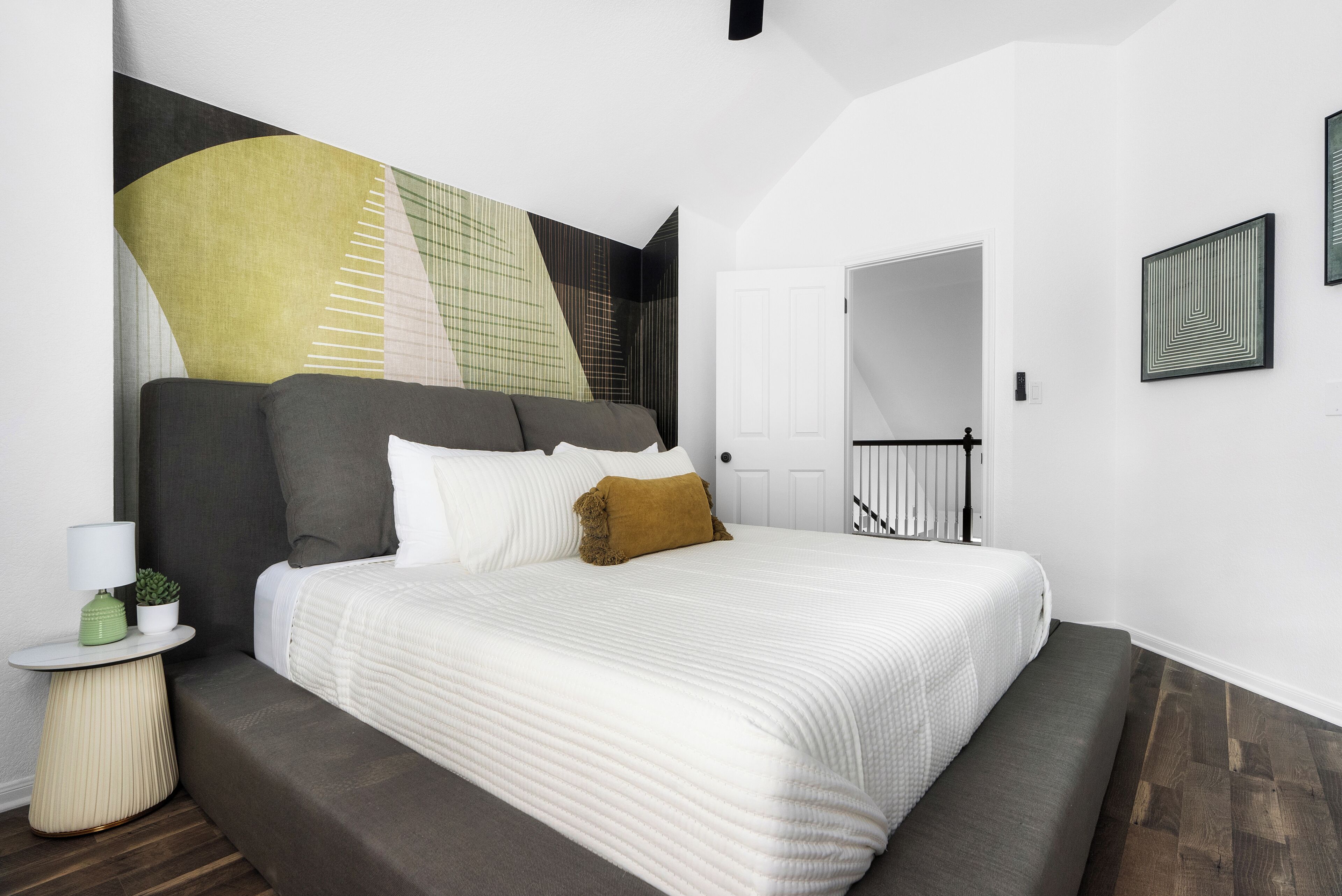 Un dormitorio moderno con una cama grande, una mesita de noche con lámpara y un espejo fijado a la pared.