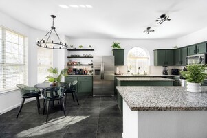 Una cocina moderna con una isla central, armarios oscuros y una araña.