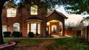 A brick house with a large front porch, a garage, and a well-maintained lawn. - Geyser Ave (Pflugerville)