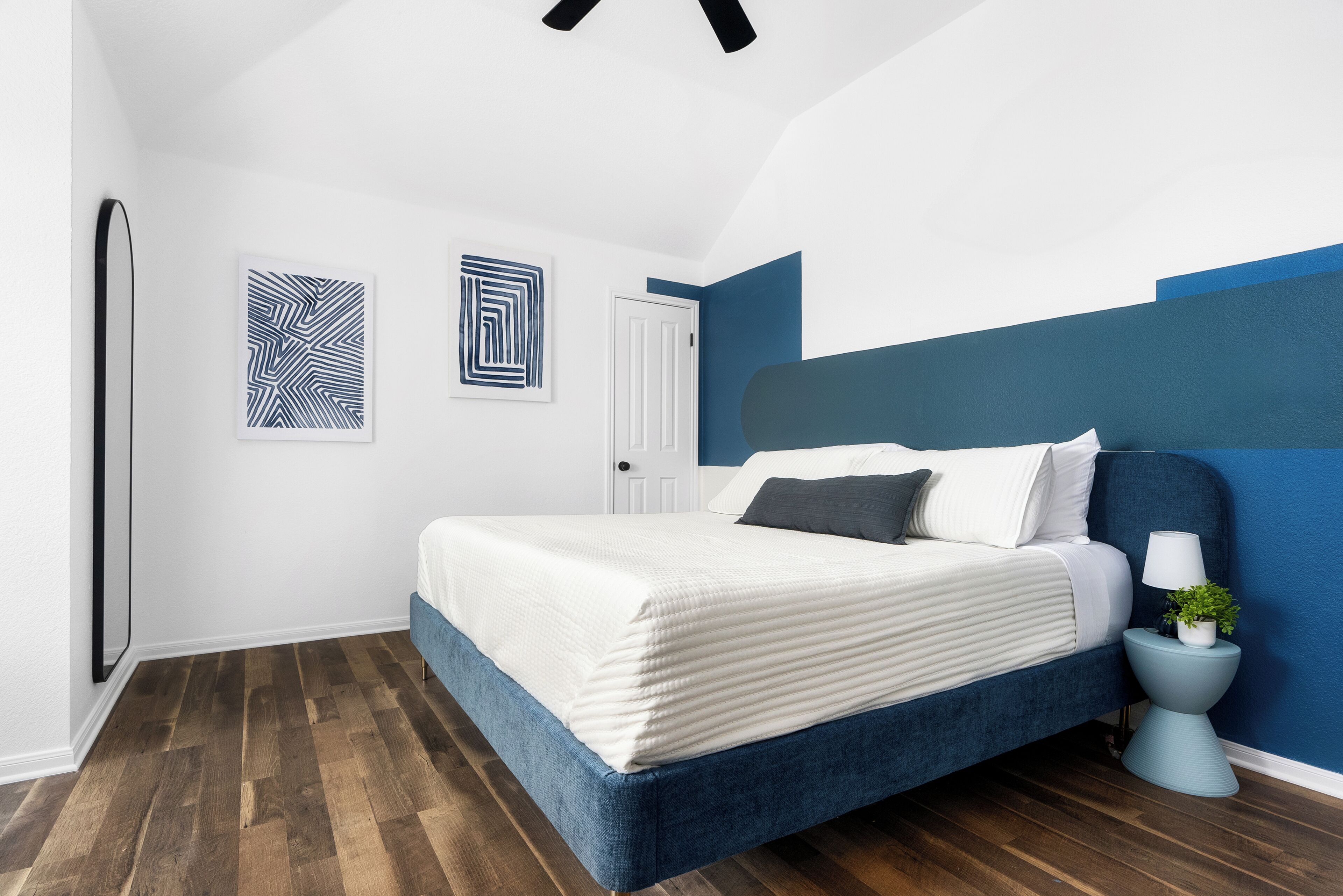 A bedroom with a bed, a nightstand, a door, and two wall art pieces.