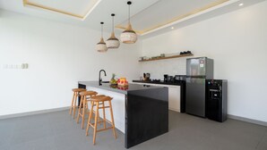 A modern kitchen with a central island, bar stools, a refrigerator, and a microwave. - Villa Kuwait Seminyak (Seminyak)