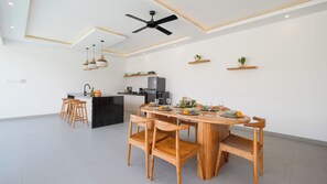 A modern kitchen with a central island, wooden dining table, and bar stools. - Villa Kuwait Seminyak (Seminyak)