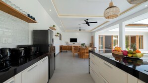 A modern kitchen with a black countertop, stainless steel appliances, and a dining area with wooden furniture. - Villa Kuwait Seminyak (Seminyak)