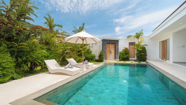 A swimming pool with lounge chairs and an umbrella, surrounded by lush greenery and modern architecture. - Villa Kuwait Seminyak (Seminyak)