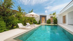 A swimming pool with lounge chairs and an umbrella, surrounded by lush greenery and modern architecture. - Villa Kuwait Seminyak (Seminyak)