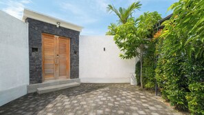 A paved courtyard with a stone wall, a wooden door, and lush greenery. - Villa Kuwait Seminyak (Seminyak)