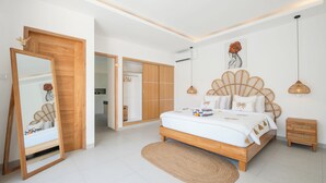 A bedroom with a bed, a wooden wardrobe, a mirror, and a hanging light fixture. - Villa Kuwait Seminyak (Seminyak)