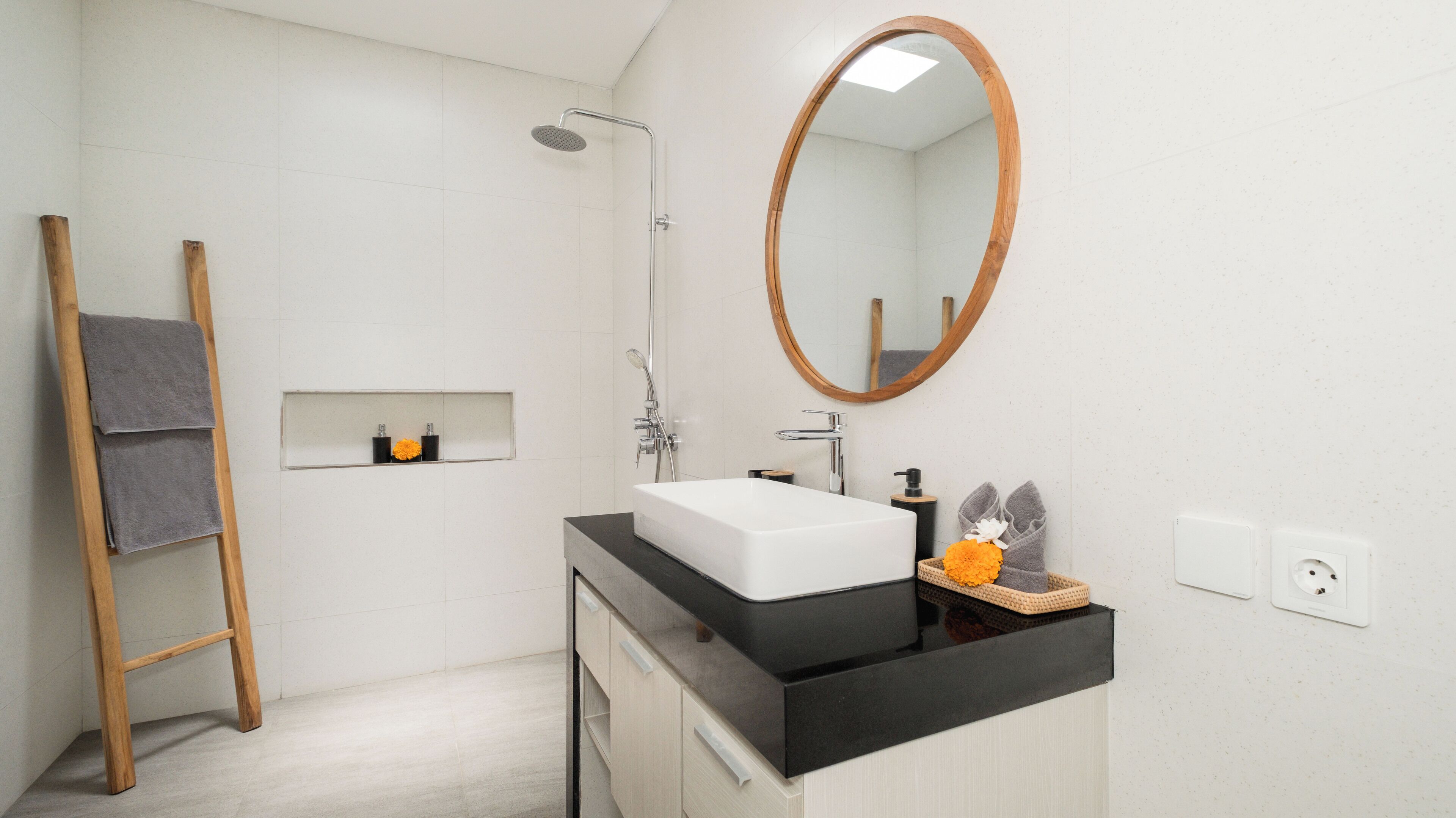 A modern bathroom with a shower, a sink with a black countertop, a wooden ladder, and a mirror.