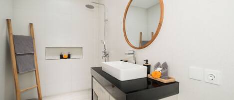 A modern bathroom with a shower, a sink with a black countertop, a wooden ladder, and a mirror.