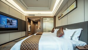 A hotel room with a large flat-screen TV, a bed with patterned bedding, a headboard, and a framed picture on the wall. - ShenZhen Romanjoy International Hotel (Shenzhen)