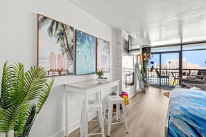 A modern hotel room with a large window, a balcony, and a beach-themed artwork on the wall. - Landmark Resort Ocean View | Beach, Pools, Lazy River (Myrtle Beach)