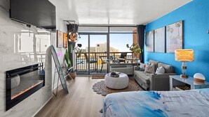A modern living room with a fireplace, a sofa, a coffee table, and a view of the city through large windows. - Landmark Resort Ocean View | Beach, Pools, Lazy River (Myrtle Beach)