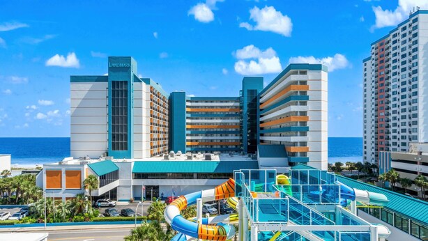 A hotel with a water park, a view of the ocean, and a parking lot with cars. - Landmark Resort Ocean View | Beach, Pools, Lazy River (Myrtle Beach)