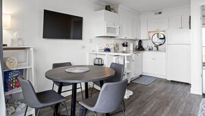 A modern kitchen with white cabinetry, a flat-screen TV, a microwave, and a coffee machine. - Boardwalk Breeze, Oceanfront, Pool! Villa (Carolina Beach)