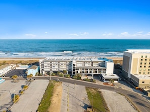 A coastal hotel with multiple floors, a parking lot, and a view of the ocean. - Boardwalk Breeze, Oceanfront, Pool! Villa (Carolina Beach)