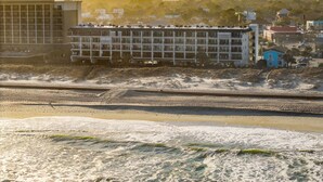 A beachfront hotel with multiple floors, a sandy beach in the foreground, and a clear sky. - Boardwalk Breeze, Oceanfront, Pool! Villa (Carolina Beach)