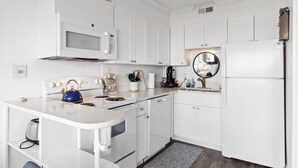 A compact kitchen with white cabinetry, a microwave, stove, and a refrigerator. - Boardwalk Breeze, Oceanfront, Pool! Villa (Carolina Beach)