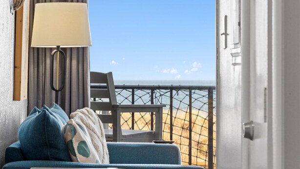 A room with a view of the beach, a sofa with cushions, a lamp, and a chair. - Boardwalk Breeze, Oceanfront, Pool! Villa (Carolina Beach)