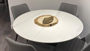 Une table ronde recouverte d’une nappe blanche, entourée de quatre chaises grises.
