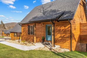 Een houten chalet met een donker dak, een blauwe deur en een klein terras.