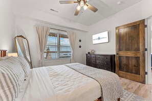 A bedroom with a bed, a dresser, a mirror, a ceiling fan, and a window with blinds. - New Cozy Lodge w Arcade_Private Hot Tub_Cmty In/Outdoor Pools & Much More_Free Attraction Tickets (Hollister)
