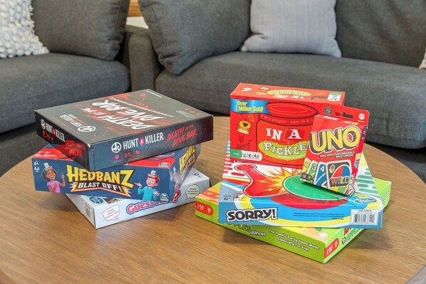 Uma mesa com diversos jogos de tabuleiro, incluindo 'HUNT & KILLER', 'HEDBANTZ', 'IN A PICKLE', 'UNO' e 'SORRY!'
