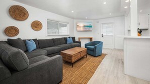 Ein modernes Wohnzimmer mit grauem Sofa, blauem Sessel, Couchtisch aus Holz und Wandgestaltung mit Gewebearbeiten.
