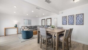 A modern dining area with a wooden table and chairs, a blue sofa, and a small side table with a lamp. - Balboa Remodeled Upstairs Unit with Parking Near the Funzone (Newport Beach)