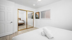 A bedroom with a bed, a large mirror, a wardrobe, and a window with blinds. - Balboa Remodeled Upstairs Unit with Parking Near the Funzone (Newport Beach)