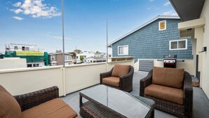 A balcony with wicker furniture, a glass table, and a barbecue grill. - Balboa Remodeled Upstairs Unit with Parking Near the Funzone (Newport Beach)