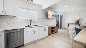 A modern kitchen with white cabinetry, a built-in dishwasher, and a large window with blinds. - Balboa Remodeled Upstairs Unit with Parking Near the Funzone (Newport Beach)