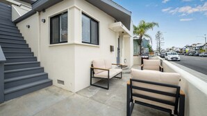 A modern building with a beige exterior, a set of stairs, and a patio area with two chairs. - Balboa Remodeled duplex with Parking Near the Funzone (Newport Beach)