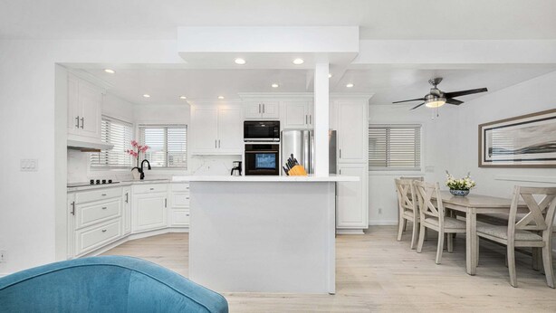 A modern kitchen with white cabinetry, a central island, and a dining area with wooden chairs. - Balboa Remodeled duplex with Parking Near the Funzone (Newport Beach)