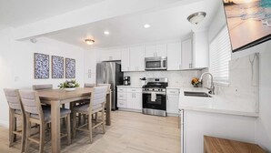 A modern kitchen with white cabinets, stainless steel appliances, and a wooden dining table with chairs. - Balboa Remodeled duplex with Parking Near the Funzone (Newport Beach)