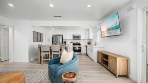 A modern kitchen with white cabinets, stainless steel appliances, and a dining area with a blue sofa and wooden table. - Balboa Remodeled duplex with Parking Near the Funzone (Newport Beach)