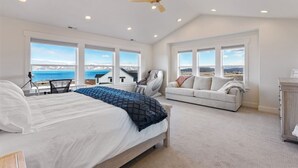 A bedroom with a bed, a chair, a sofa, and large windows with a view.