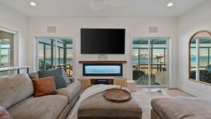 A modern living room with a flat-screen TV, comfortable seating, and a view of the outdoors.