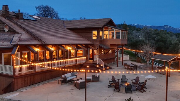 Une maison en bois avec une terrasse, un espace salon extérieur et une vue sur les montagnes.