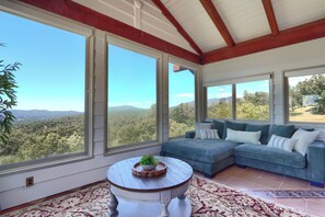 A room with a large window, a sofa, and a small table with a plant. - NEW! Luxury Yosemite Estate-Pool-Hot Tub- 5BR 4.5BA-Sleeps 16-55 Private Acres. (Oakhurst)