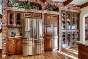 A kitchen with a stainless steel refrigerator, wooden cabinets, and a brick fireplace. - NEW! Luxury Yosemite Estate-Pool-Hot Tub- 5BR 4.5BA-Sleeps 16-55 Private Acres. (Oakhurst)