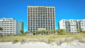 A beachfront hotel with multiple floors, a sandy foreground, and a clear blue sky. - Beachfront Paradise - Stunning views - Stargazzing (Myrtle Beach)