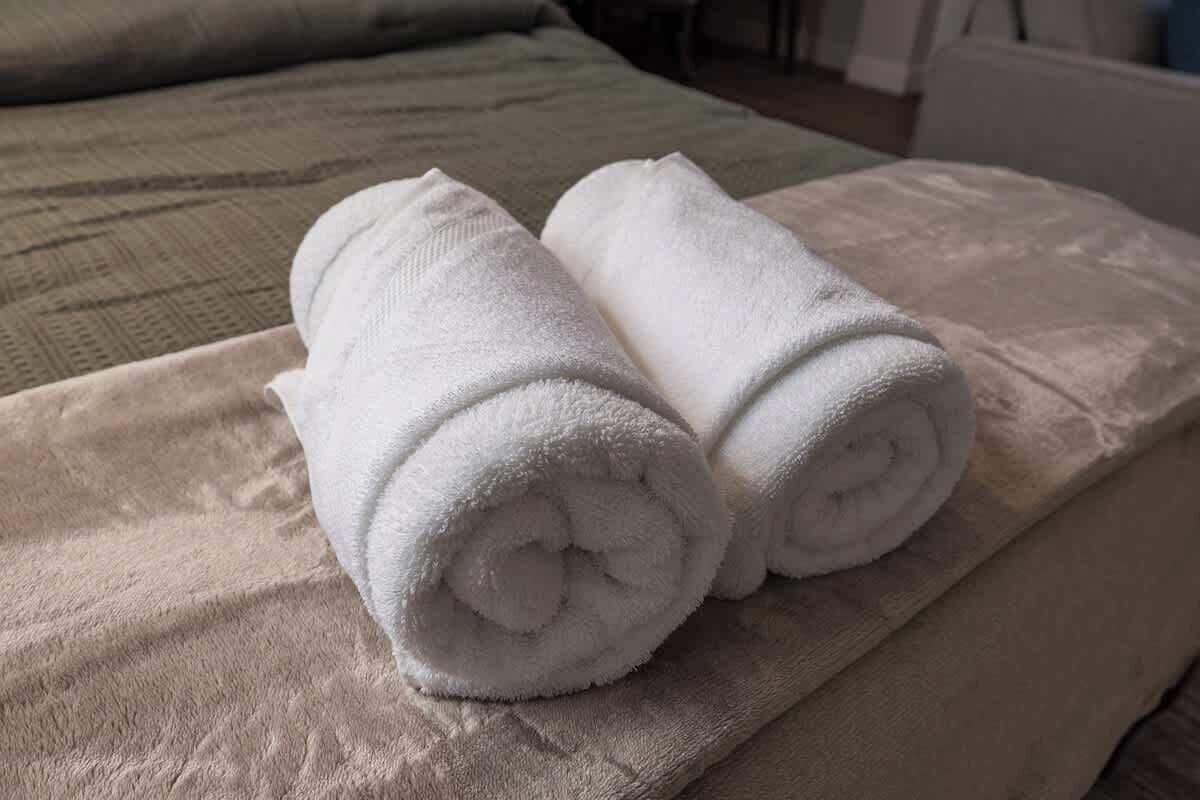 Two rolled white towels on a beige bedspread in a hotel room.