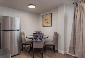 A compact kitchen with a stainless steel refrigerator, a round dining table with four chairs, and a wall-mounted painting. - Modern Downtown Studio - King Bed - Inlet Views (Anchorage)
