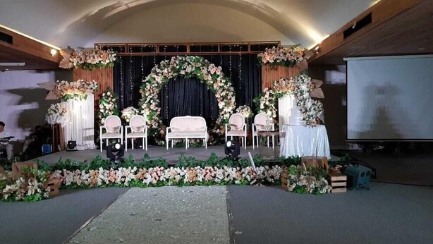 An indoor event space with a stage, chairs, and floral decorations.