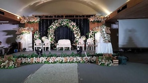 En inomhuslokal som används för evenemang, med en scen, stolar och blomsterdekorationer.