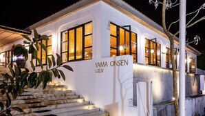 A modern building with the name 'YAMA ONSEN' on the facade, featuring large windows and a staircase leading to the entrance.
